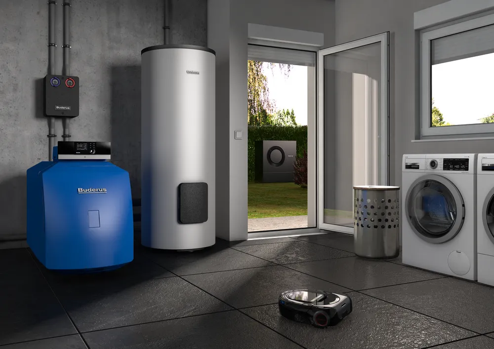 Moderner Heizungsraum mit Buderus Öl-Brennwertkessel, Warmwasserspeicher, Waschmaschine und Wäschetrockner, mit Blick auf Wärmepumpe im Garten durch geöffnete Tür.