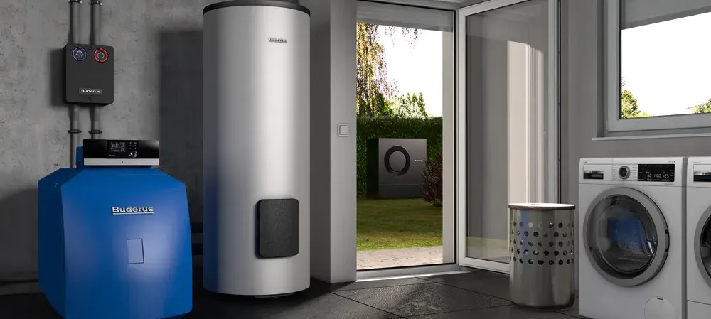 Moderner Heizungsraum mit Buderus Öl-Brennwertkessel, Warmwasserspeicher, Waschmaschine und Wäschetrockner, mit Blick auf Wärmepumpe im Garten durch geöffnete Tür.